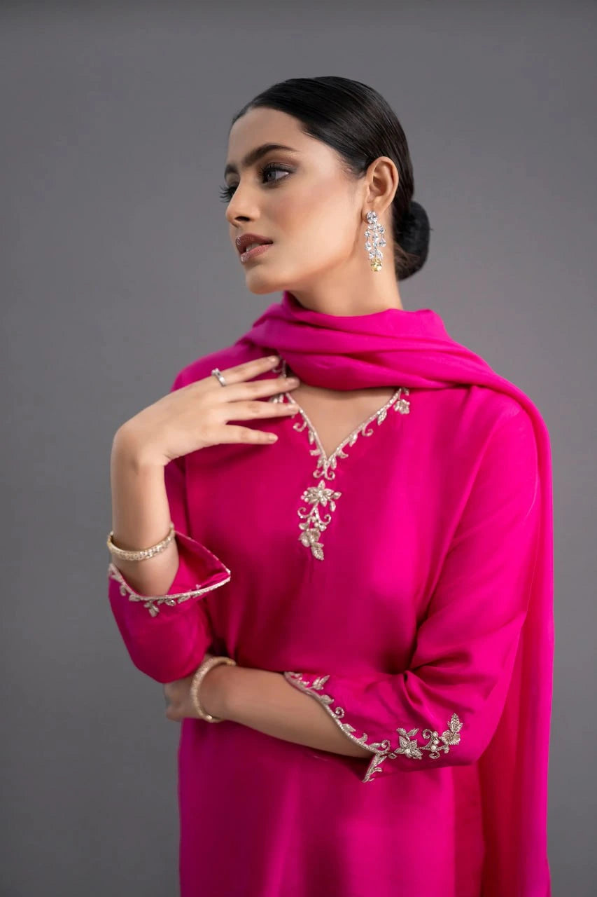 Woman wearing a bright pink traditional outfit with intricate designs on a gray background
